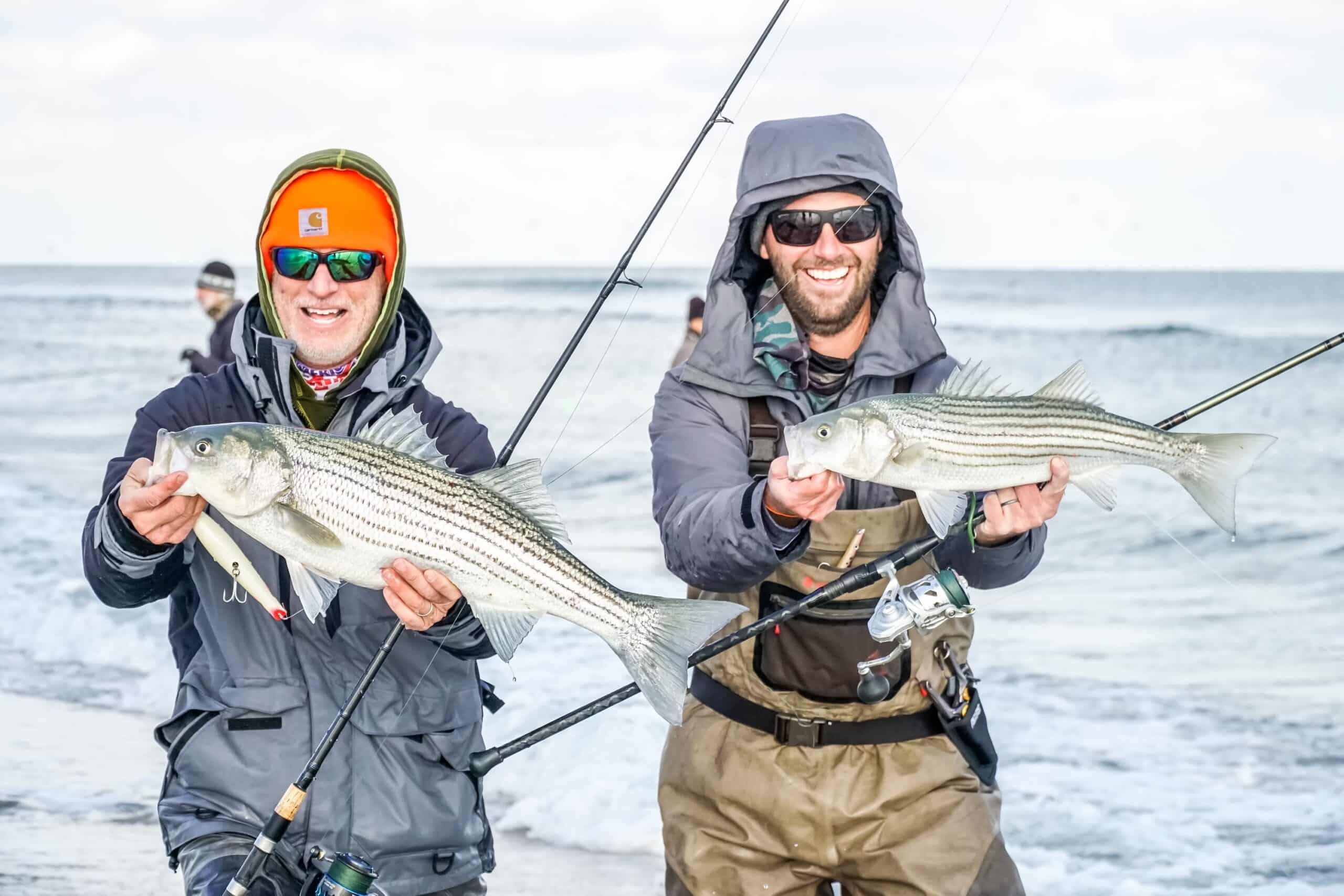 two men hold fish in front of ocean