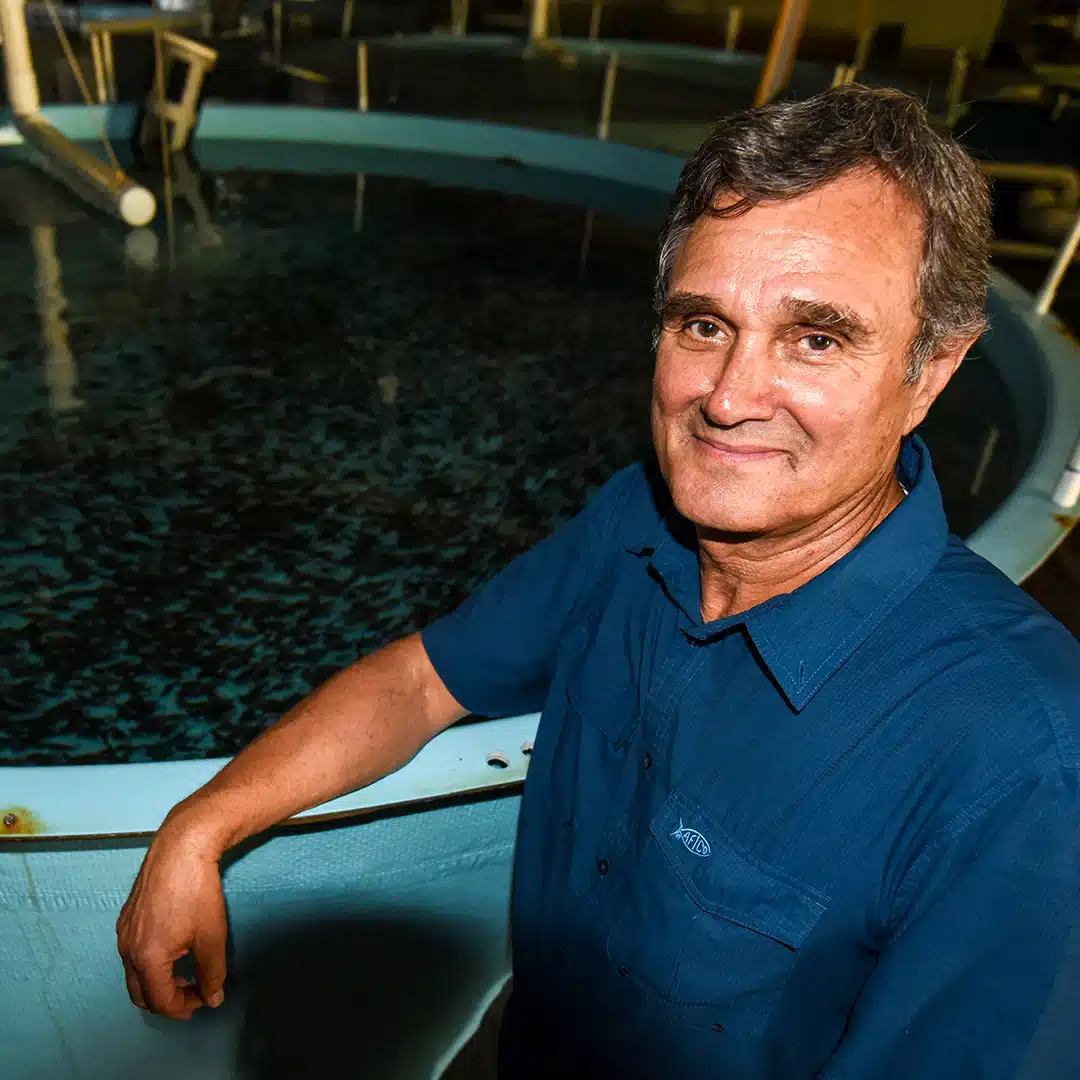 A person in a blue shirt stands next to a large circular fish tank filled with water.